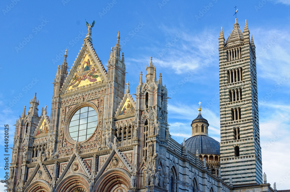 The main facade, the dome and the tower of the Cathedral of Siena Duomo under a few clouds and a blue sky