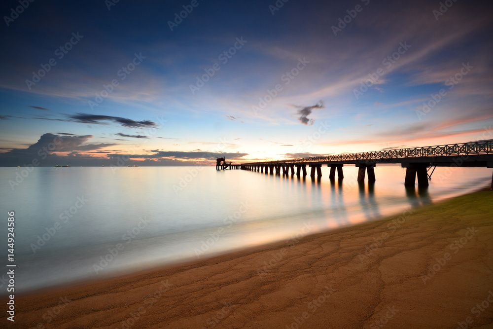 Long exposure shot of seascape with long jetty background at dusk.