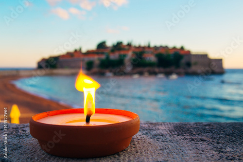 Burning candle on the beach against the background of Sveti Stefan in Montenegro