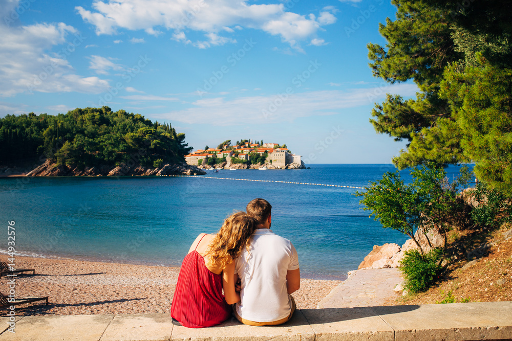 A young couple hugs and looks at the island of Sveti Stefan in Montenegro.