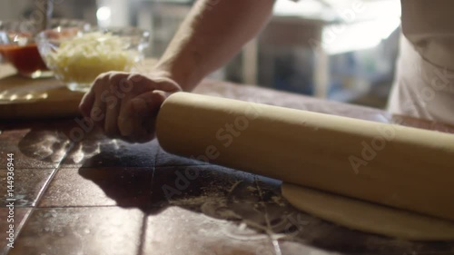 Tracking closeup shot in slow motion of hands of chef rolling dough on floury table in restaurant kitchen photo