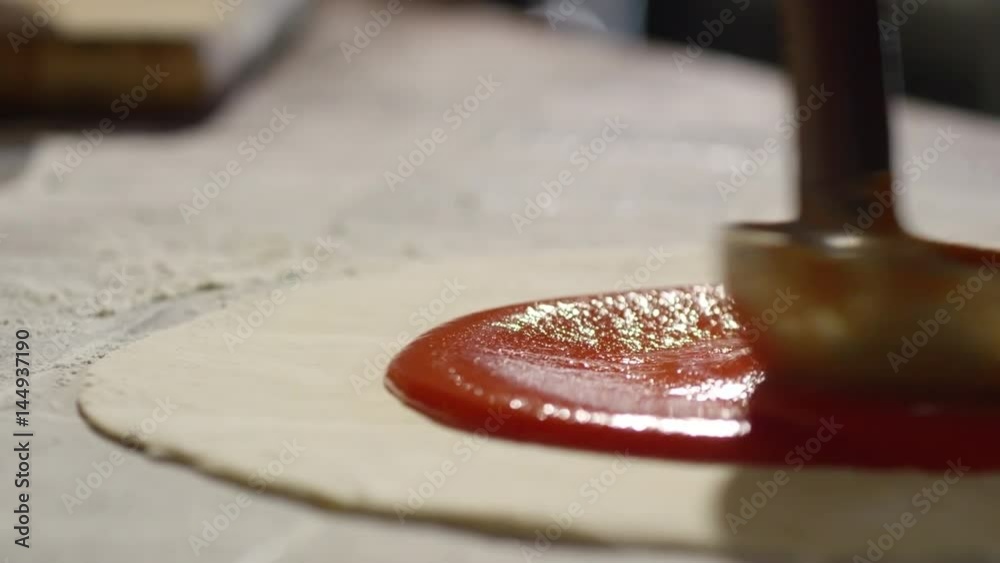 Tracking slow motion shot of applying tomato ketchup with metal ladle on pizza base
