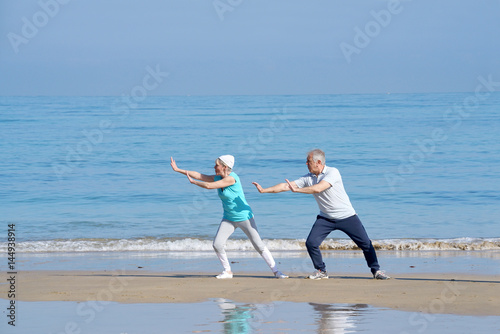 Senior couple doing stretching exercices on the beach