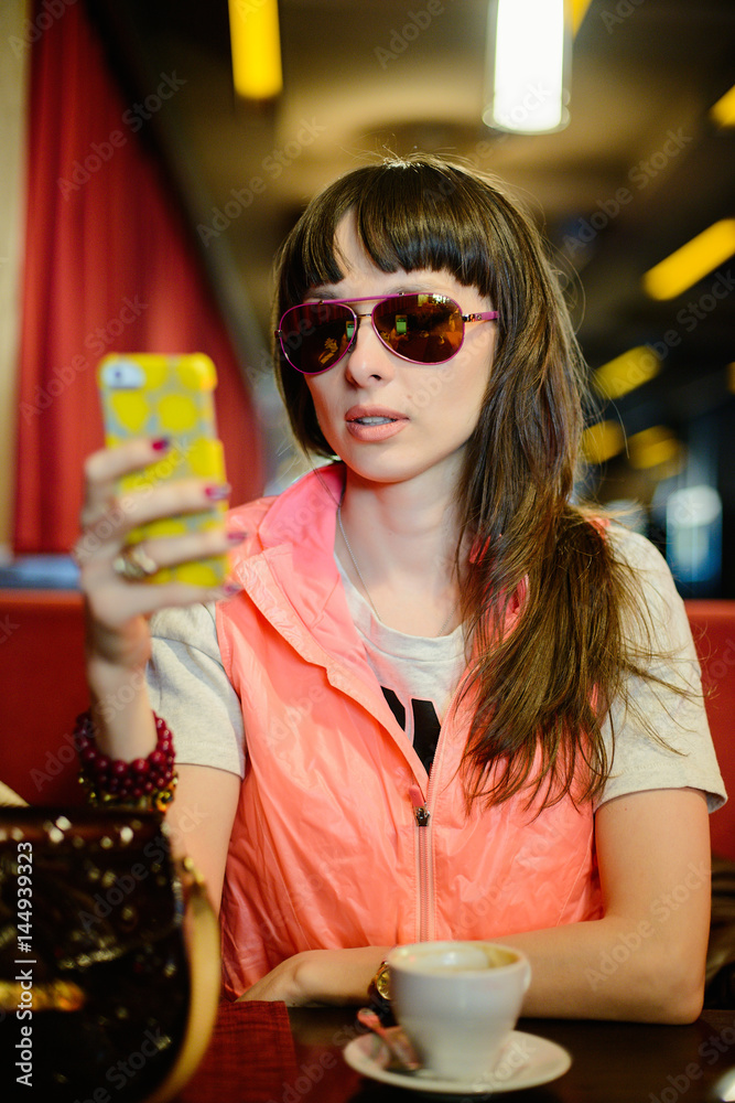 fashionable girl in dark glasses with a phone in a cafe looking at phone, on a dark cozy background