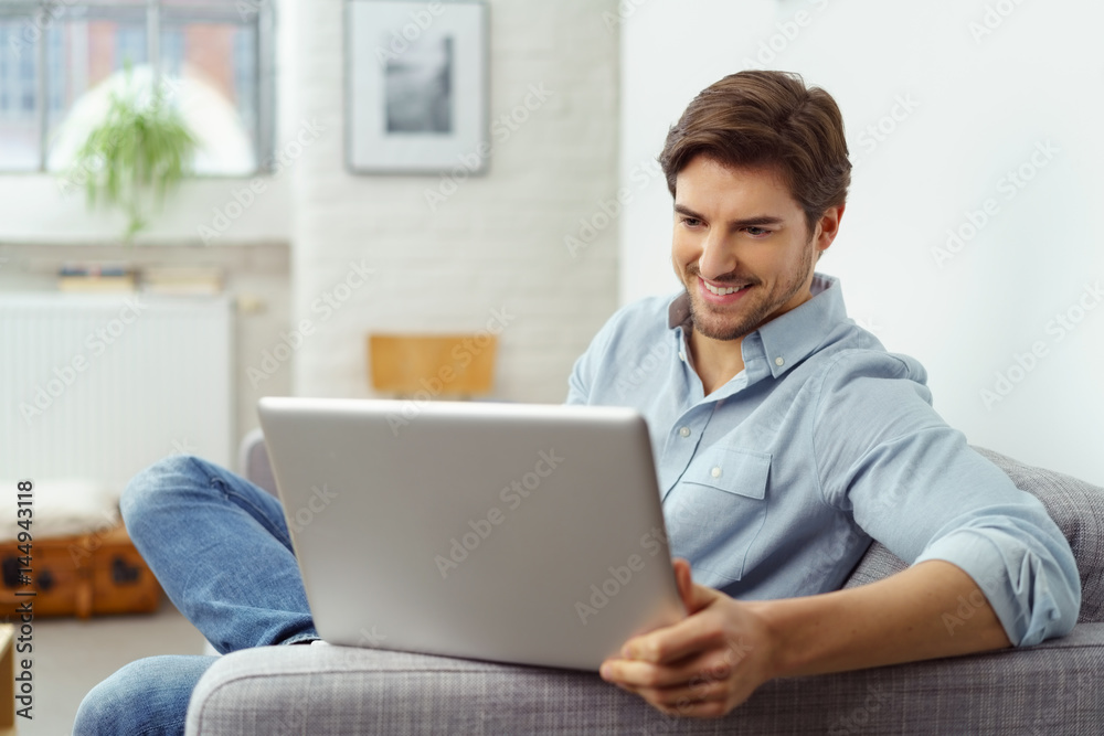 mann sitzt zuhause auf dem sofa und schaut auf seinen laptop