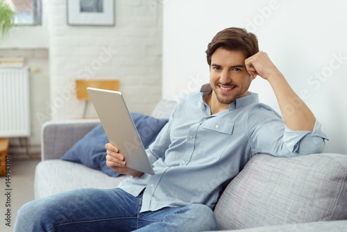 lächelnder mann sitzt auf dem sofa und hält ein tablet in der hand