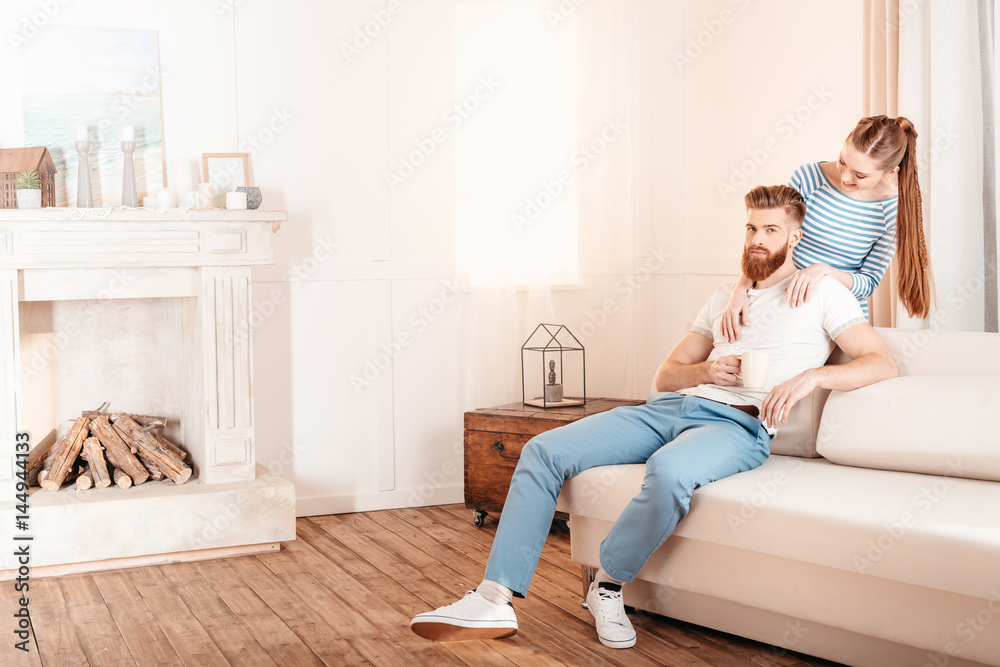 Beautiful young woman hugging handsome bearded man sitting on sofa at home Beautiful young woman hugging handsome bearded man sitting on sofa at home