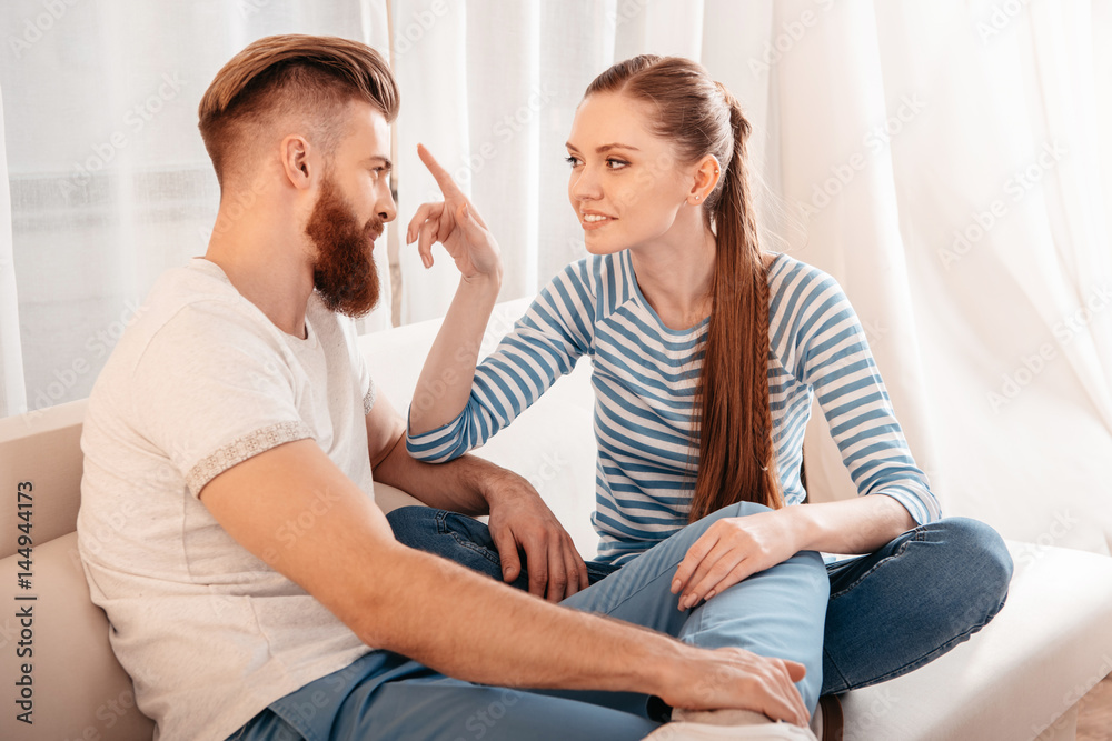 Obraz premium Happy young couple sitting together on sofa and looking at each other
