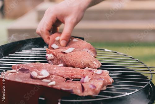 man roasting meat with onion on barbecue grill