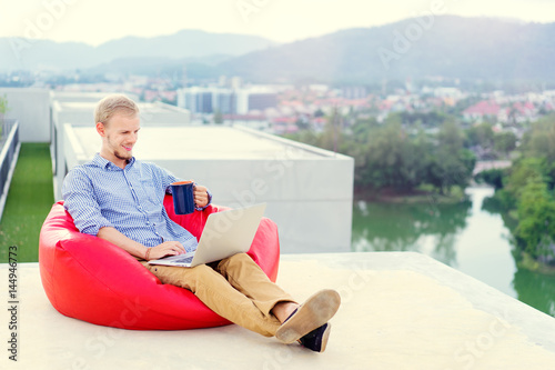 Freelance businessman. Young handsome man working on laptop while sitting on the roof top.