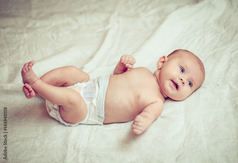 happy baby lying on white sheet and holding his legs happy baby lying on white sheet and holding his legs