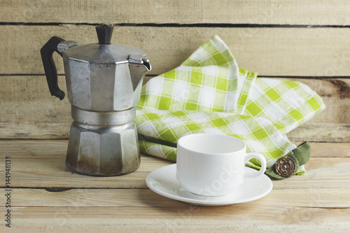 Cup on the saucer, coffee pot and plaid napkin, wooden background