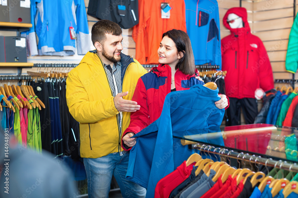 Fototapeta premium Couple examining track jackets in sports clothes store