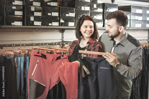 Young couple choosing touristic trousers in sports clothes store