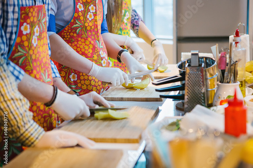 Many cooks prepare food; Hands in rubber gloves cut food on a cutting board. Workshop