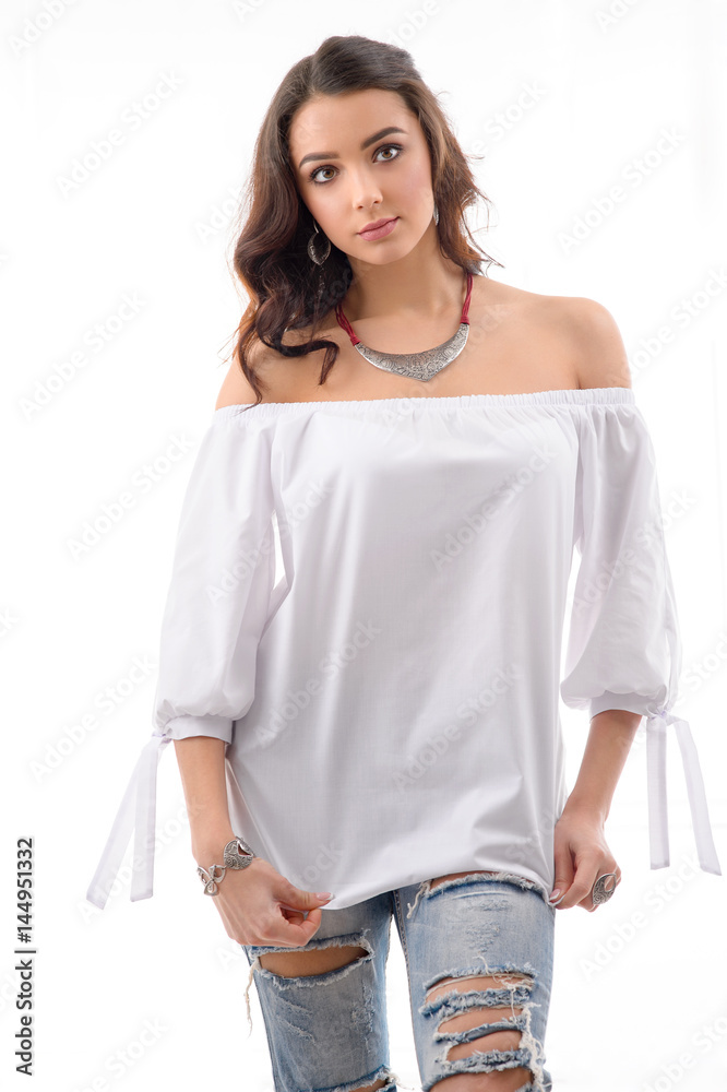 Fashionable looking model wearing white dress with Ripped Jeans and jewellery  with silver accessory posing at studio location. Stock Photo | Adobe Stock