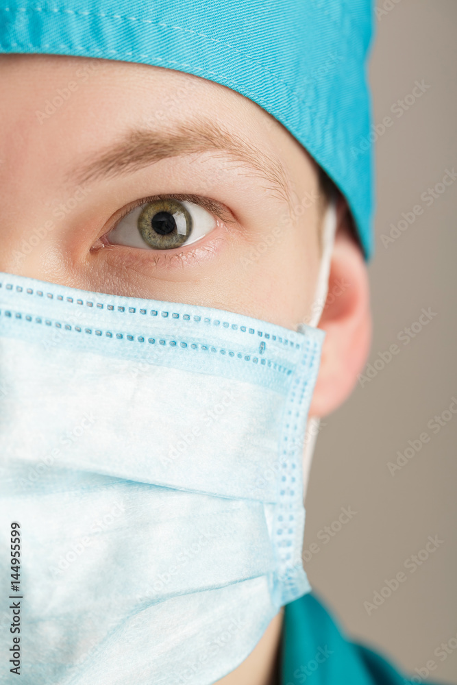 male surgeon in mask looking at camera on grey background, close up