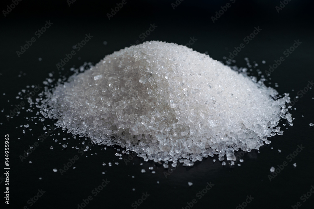 Heap of granulated white sugar on black surface Heap of granulated white sugar on black surface