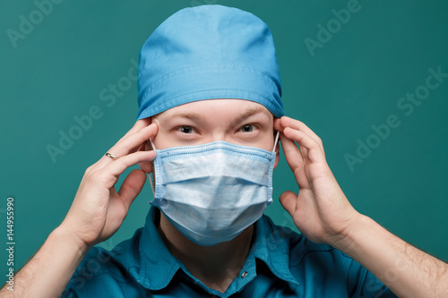 tired male surgeon in mask on blue background, close up