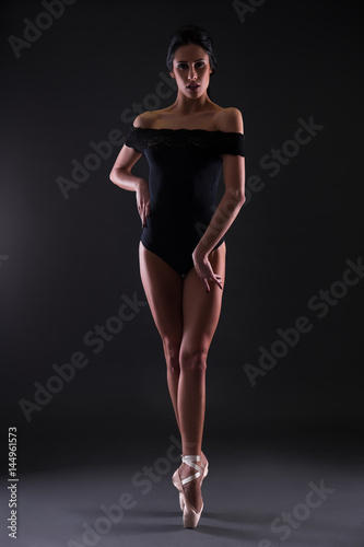 beautiful woman ballerina in black body suit posing on toes over black