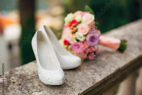 bride's shoes lie on the green grass in the forest next to a wedding bouquet of flowers and greenery