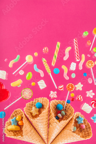Close-up top view of waffle cones and mix of various sweets on pink background