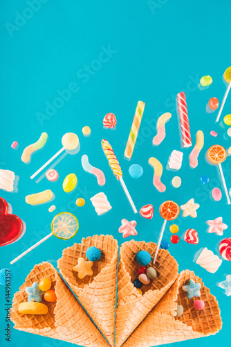 Close-up top view of waffle cones and mix of various sweets on blue background