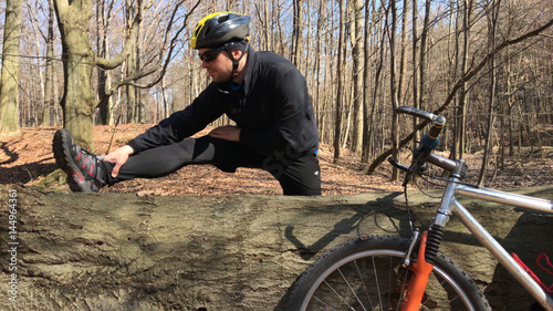 Biker doing his warm-up on nature trail, standing beside bike.