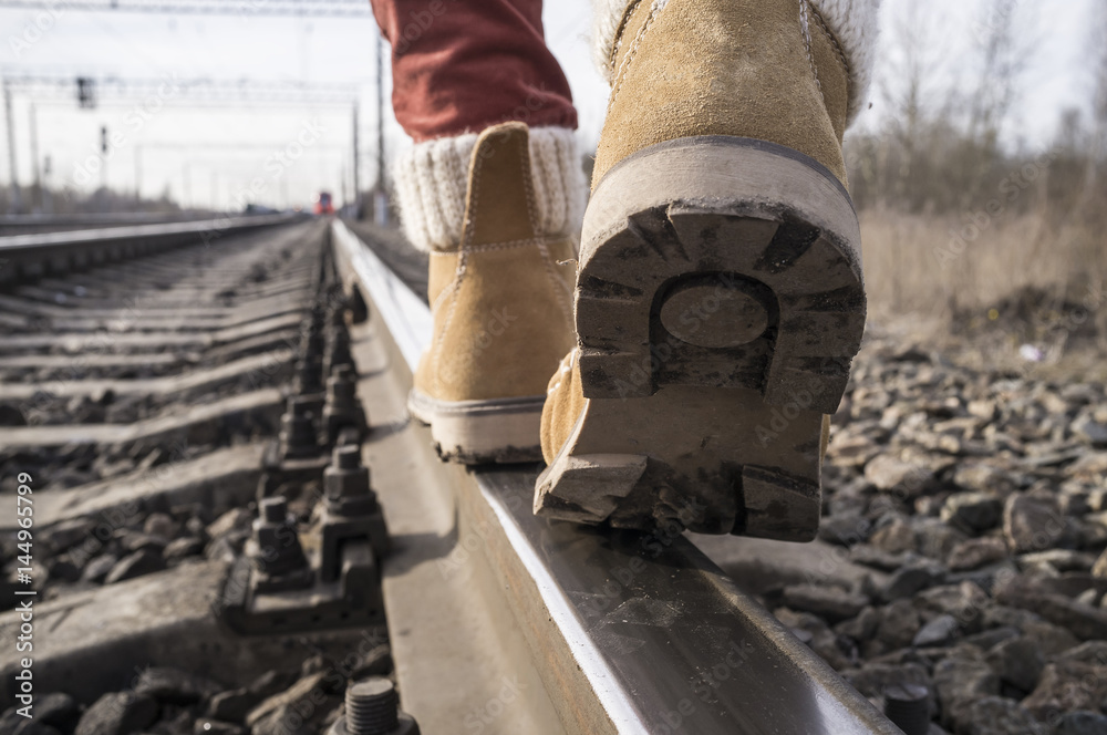 Legs in stylish boots go on rails on the railway, against the background of the approaching train. Close-up. Legs in stylish boots go on rails on the railway, against the background of the approaching train. Close-up.