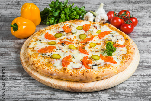 Pizza meat with cheese and cucumber, with rosemary and spices on a light wooden background. Italian pizza on a background of green basil and fresh vegetables