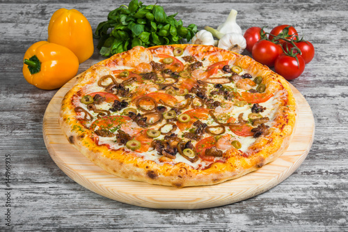 Pizza with seafood, with rosemary and spices on a light wooden background. Italian pizza on a background of green basil and fresh vegetables