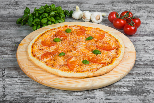Thin pizza with tomatoes and cheese, rosemary and spices on a light wooden background. Italian pizza on a background of green basil and fresh vegetables