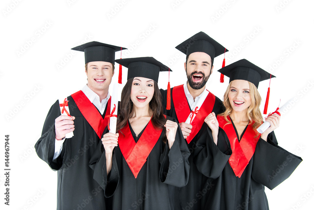 Happy young students in academic caps holding diplomas and smiling at camera Happy young students in academic caps holding diplomas and smiling at camera