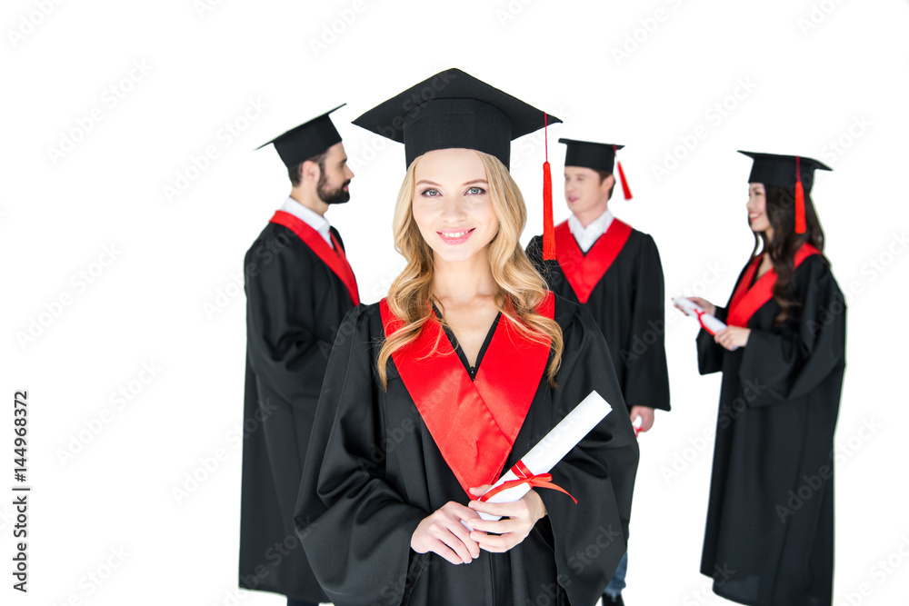 Happy young woman in mortarboard holding diploma and friends standing behind