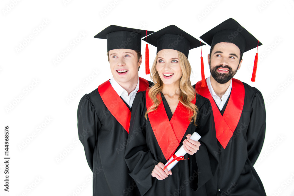 Happy students in mortarboards and graduation gowns looking away on white Happy students in mortarboards and graduation gowns looking away on white