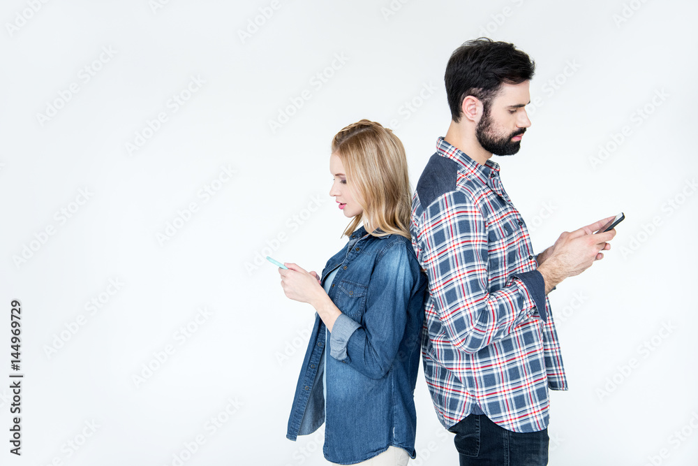 man and woman using smartphones and standing back to back on white man and woman using smartphones and standing back to back on white