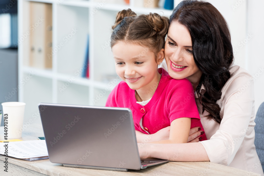 Beautiful happy mother and daughter using laptop at workplace Beautiful happy mother and daughter using laptop at workplace