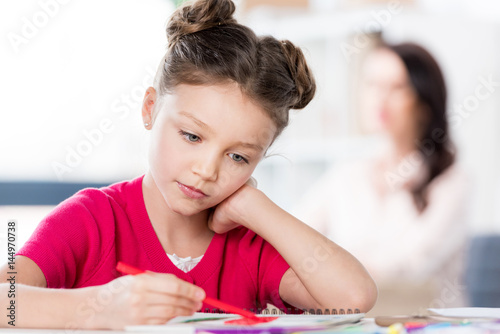Pensive little girl sitting at table and drawing with pen