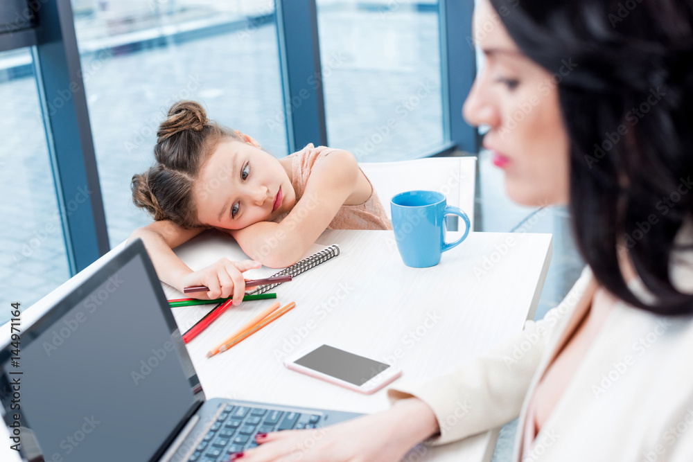 businesswoman working with laptop while her daughter drawing behind in office businesswoman working with laptop while her daughter drawing behind in office