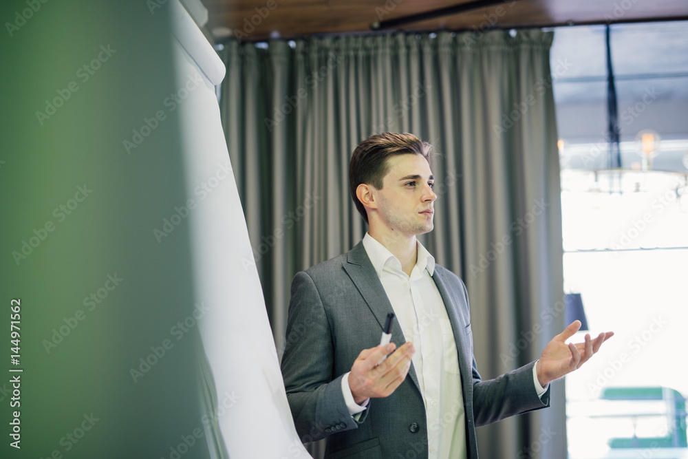 Confident young team leader or manager standing in front of a flip chart and present project on office Confident young team leader or manager standing in front of a flip chart and present project on office