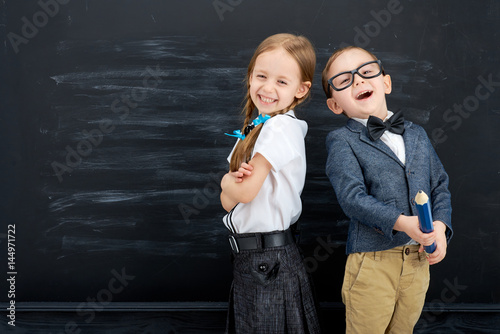 Little girl and boy against blackboard. School concept