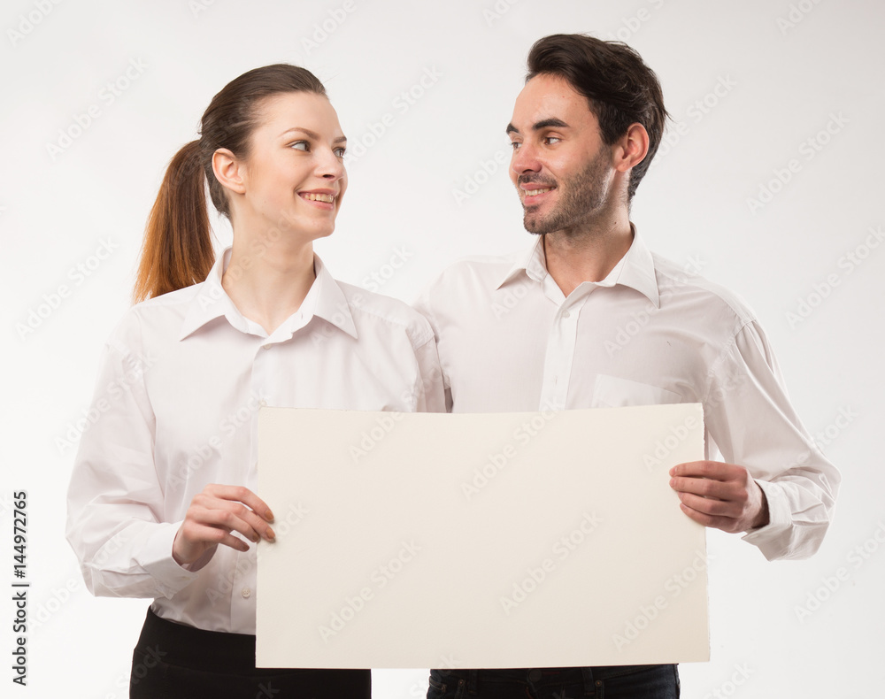 Young happy couple showing presentation pointing on placard over gray background Young happy couple showing presentation pointing on placard over gray background