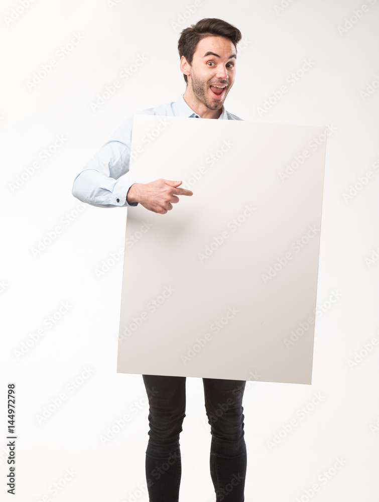 Young happy man showing presentation, pointing on placard over gray background Young happy man showing presentation, pointing on placard over gray background