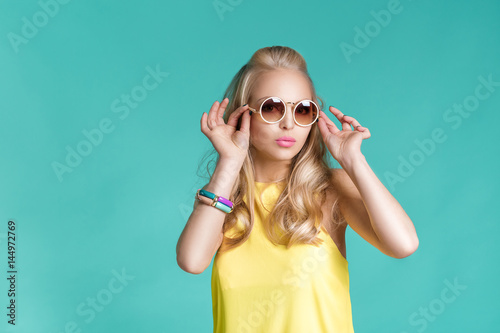 portrait of beautiful blond woman in sunglasses and yellow shirt on blue background. Carefree summer.