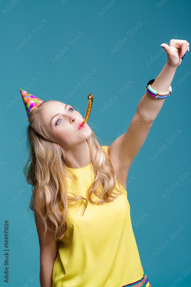 portrait of funny blond woman in birthday hat and yellow shirt on blue background. Celebration and party. portrait of funny blond woman in birthday hat and yellow shirt on blue background. Celebration and party.