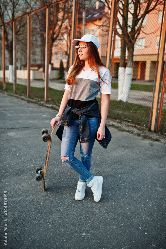 Young teenage urban girl with skateboard, wear on glasses, cap and ripped  jeans at the yard sports ground. Stock Photo | Adobe Stock