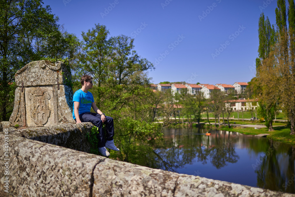 Hombre joven sentado en el exterior del puente romano de Allariz