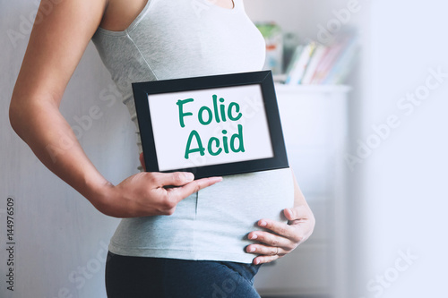 Pregnant woman holds whiteboard with text message - FOLIC ACID.
