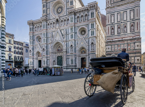 A traditional horse carriage passes near the Duomo in Florence, Italy, on a sunny day