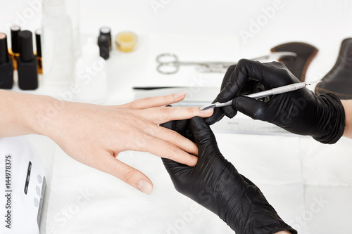 Manicrurist in gloves pushing cuticle on woman's ring finger.